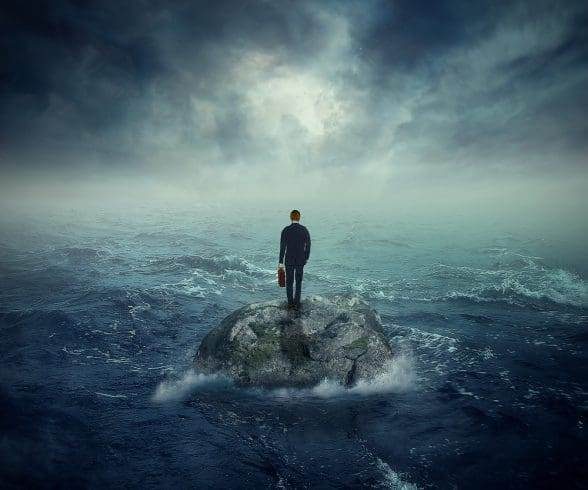 A man standing on a rock in the middle of the ocean and thinking of a way to survive.