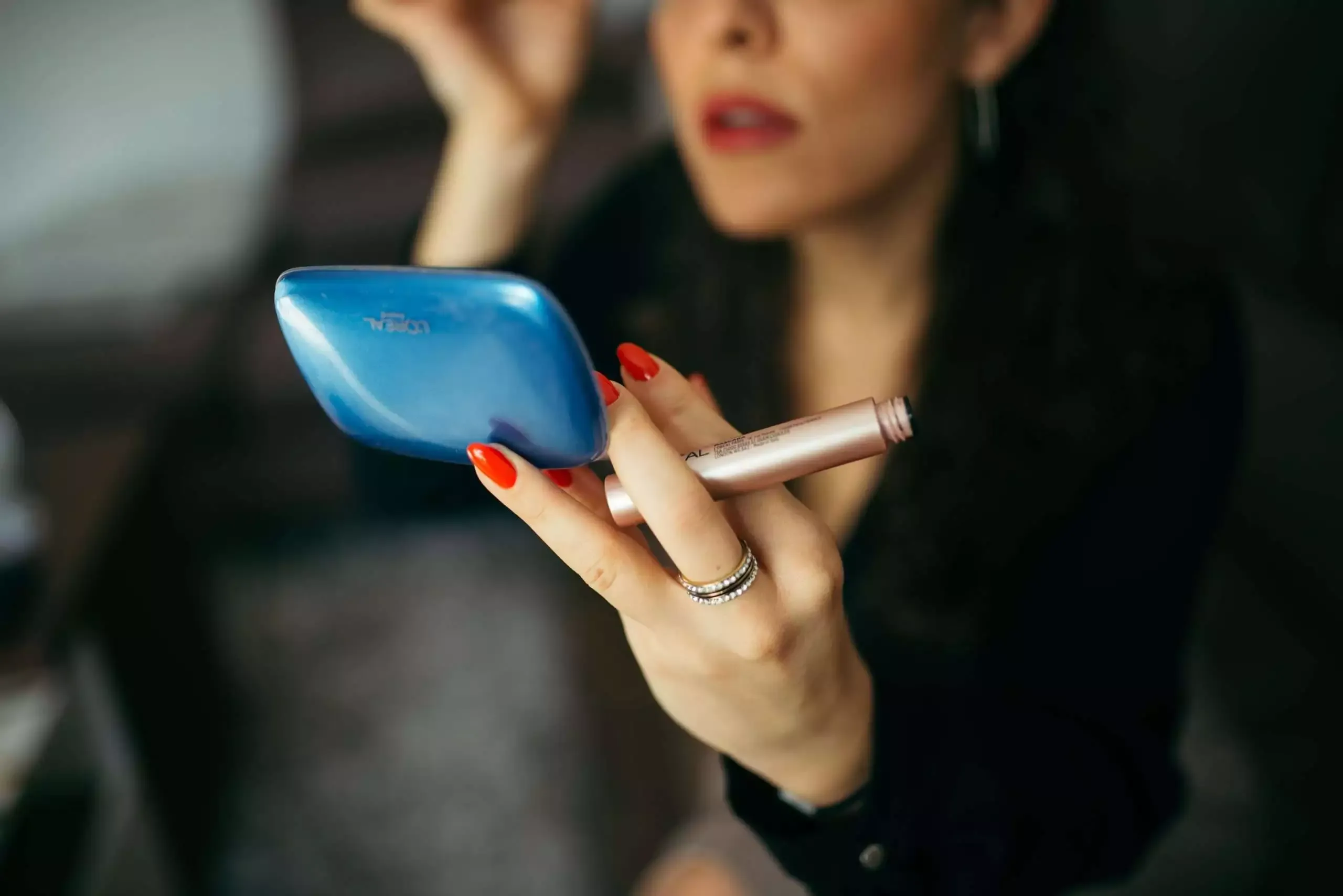 How to do Makeup Step by Step with 15 Amazing Products 9 Close-up of a woman with red nail polish holding a mirror and mascara in the same hand