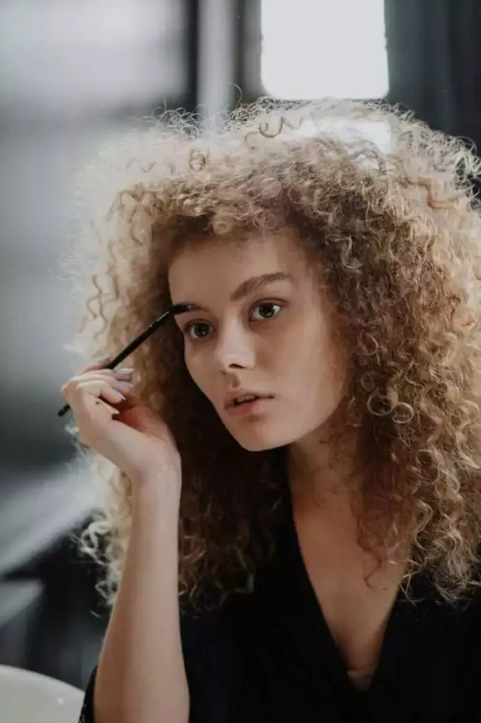 How to Do Makeup at Home (Best Guide of 2022) 16 Woman combing her eyebrows