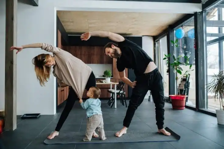 10 Benefits of Morning Exercise for Students 8 Family doing yoga. Mother and father doing side tilts as a part of their morning exercise, while their child pulling mother's shirt, seeking attention.
