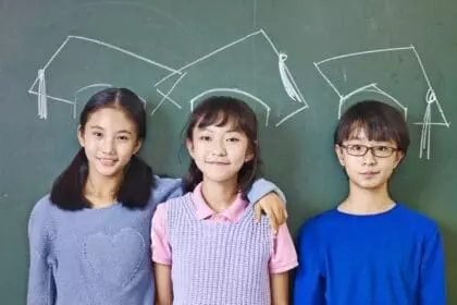 three Asian elementary school children standing in front of chalkboard underneath chalk-drawn doctoral caps. how to become successful after high school