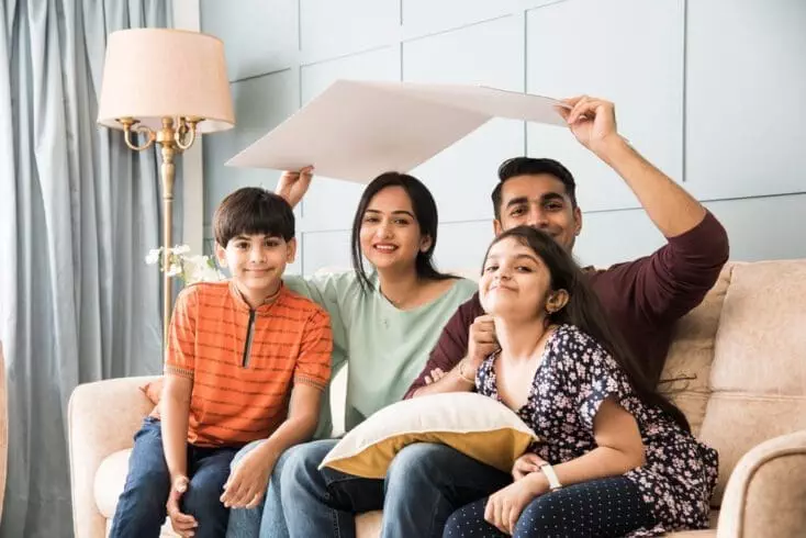 Reason why indians live with their parents. Indian family father, mother, son and daughter holding house roof made of cardboard - real istate concept in india