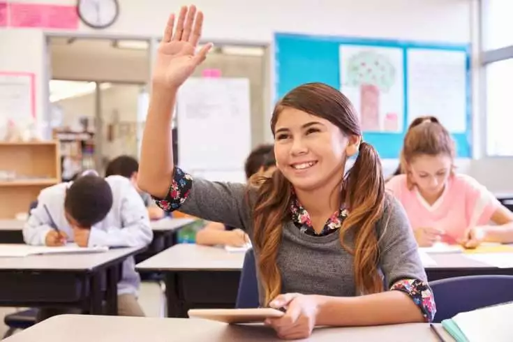 Young student raising her hand in the classroom