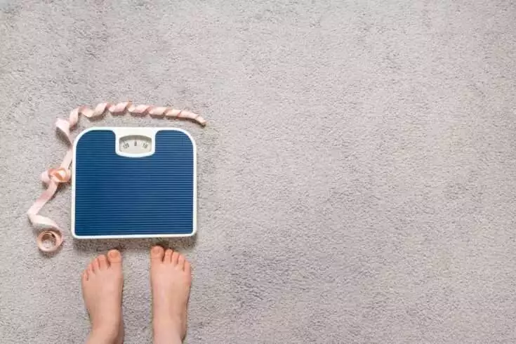 Bare feet and a floor blue scale with a measuring centimeter tape, the concept of losing weight, place for text, top view.