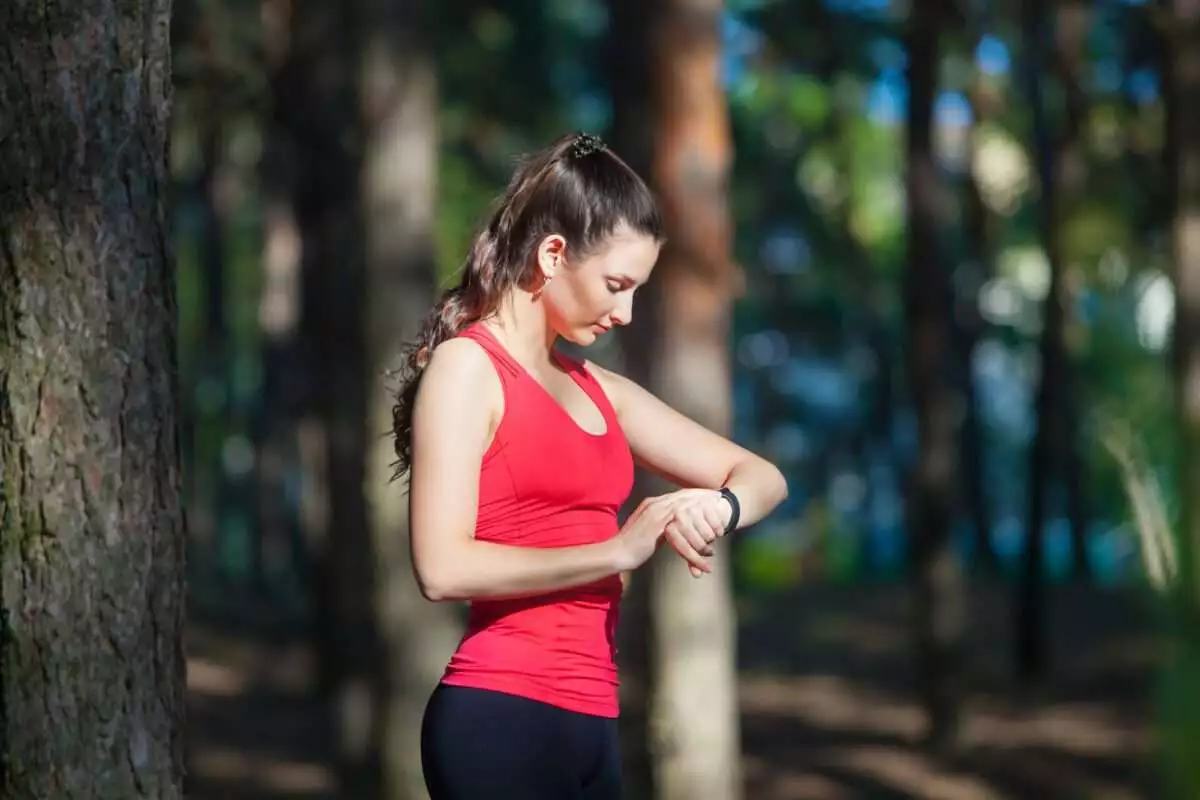 Beautiful woman runner looks at her fitness tracker getting ready for a run in the summer forest. Source: Depsoitphotos