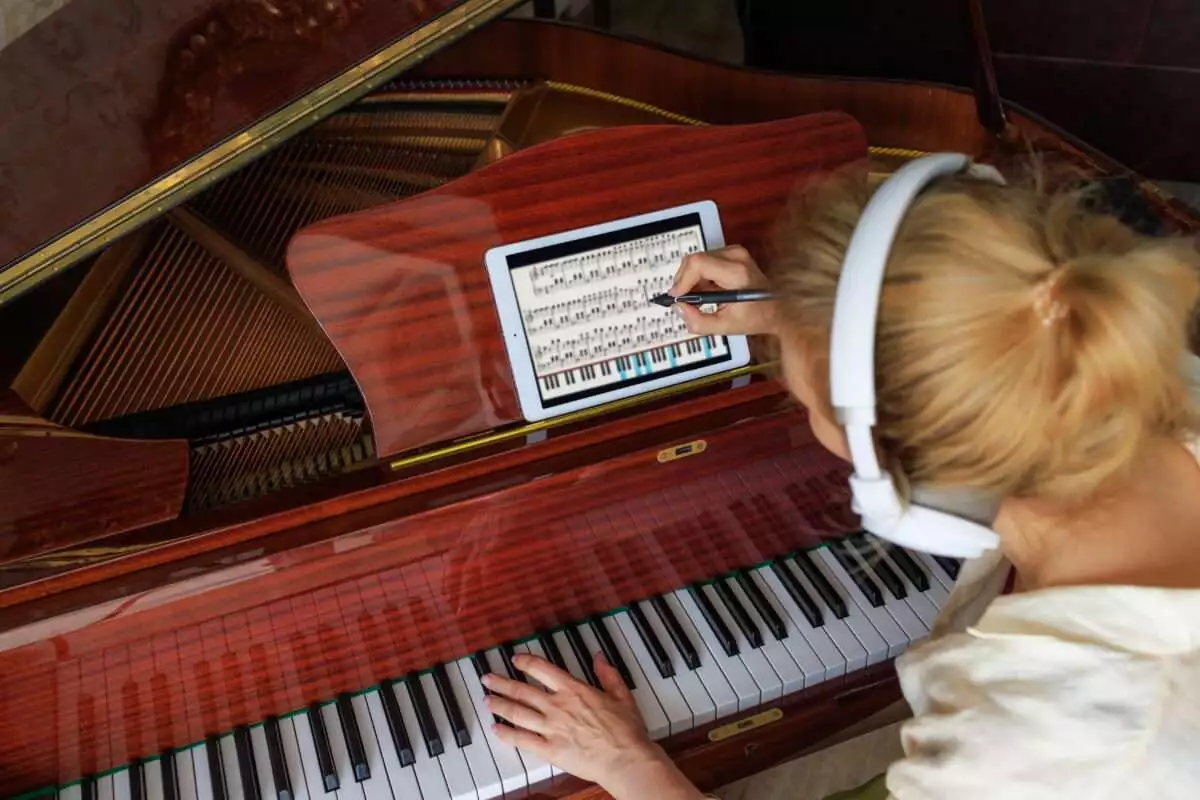 how to read music : a young girl composer, writes music on a tablet and plays the piano. Modern concept